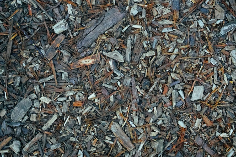 A close-up shot of a garden fork turning and aerating a pile of dark, organic mulch.