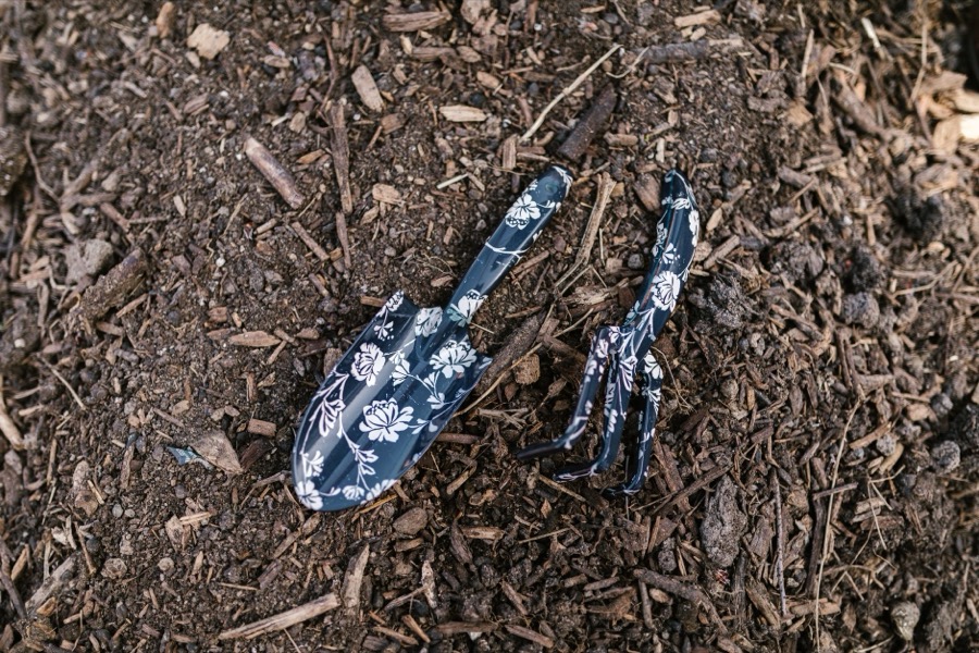Gardener using a pitchfork to turn and aerate dark brown mulch in a garden bed.